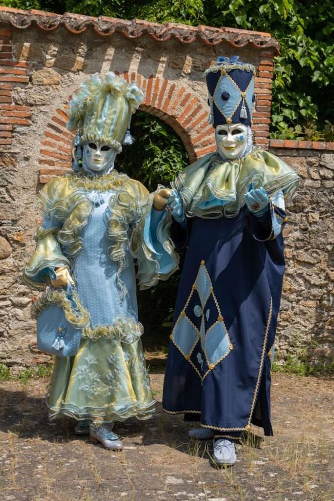 Two adults in ornate carnival costumes posing outdoors in Clisson, France.