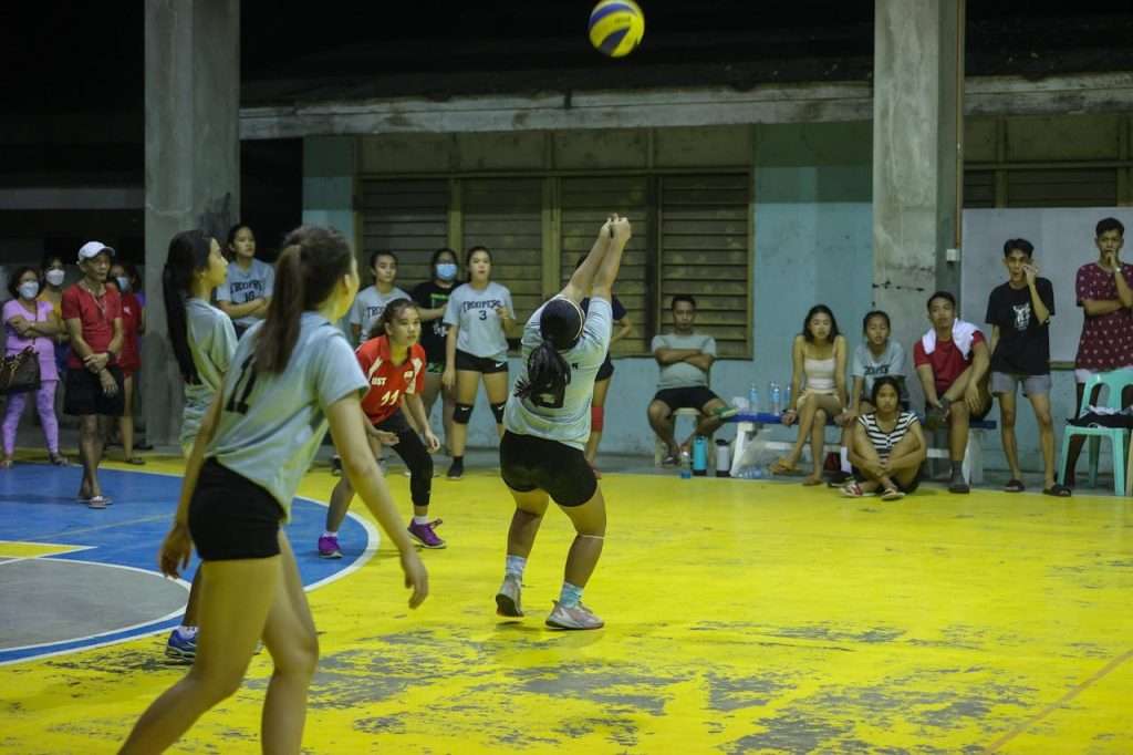 group-of-women-playing-volleyball-12394044 Women playing volleyball indoors with a lively crowd watching, showcasing teamwork and sportsmanship.